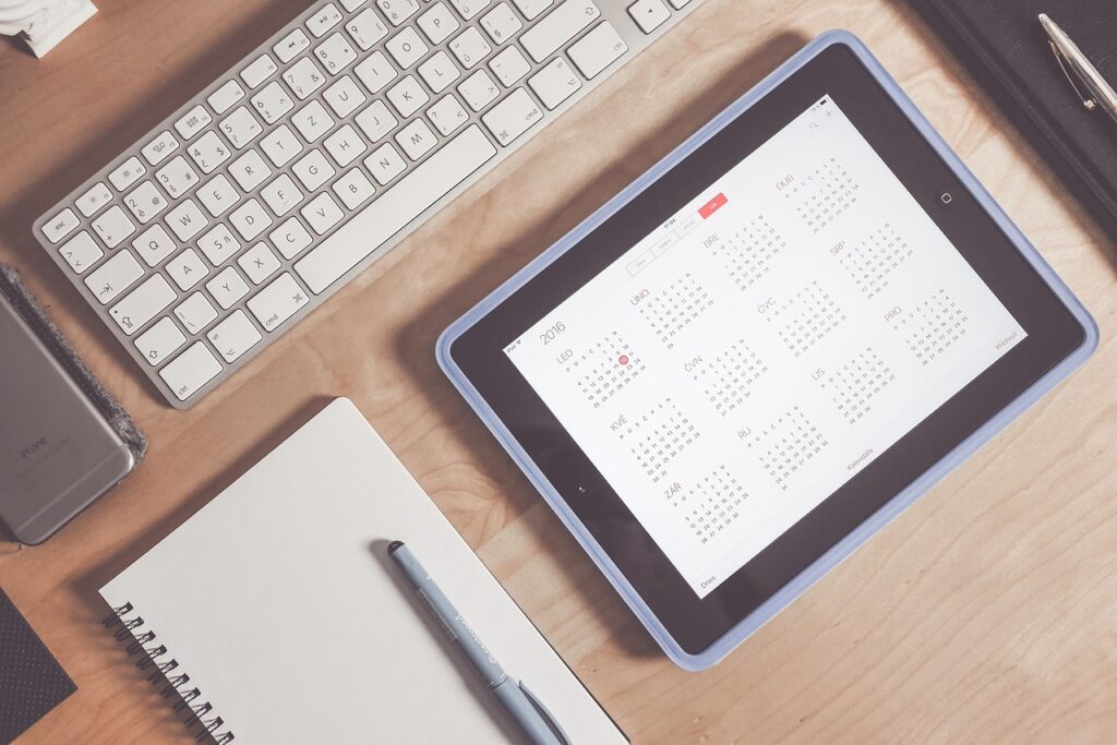 Workspace with a tablet showing a calendar, a notebook, a pen, and a keyboard, symbolizing the organization of a Japanese study routine.