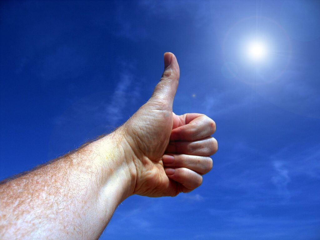 A close-up of a hand giving a thumbs-up against a bright blue sky, symbolizing positivity and encouragement.