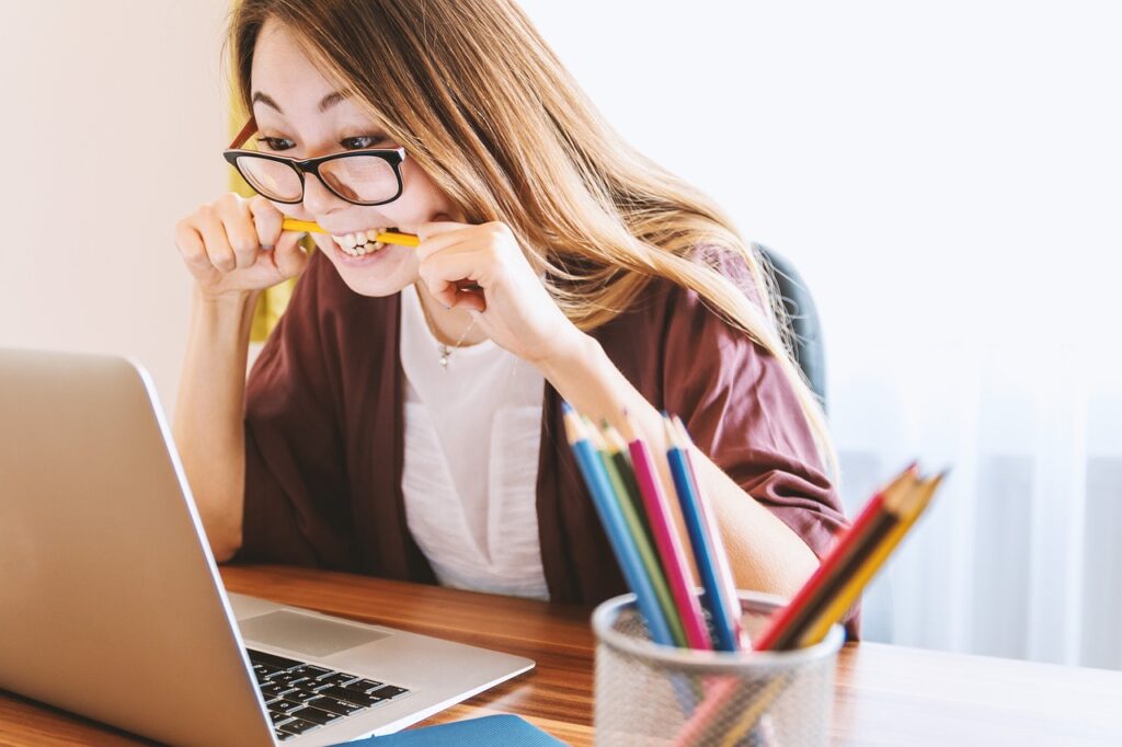 Woman biting a pencil while working on a laptop.