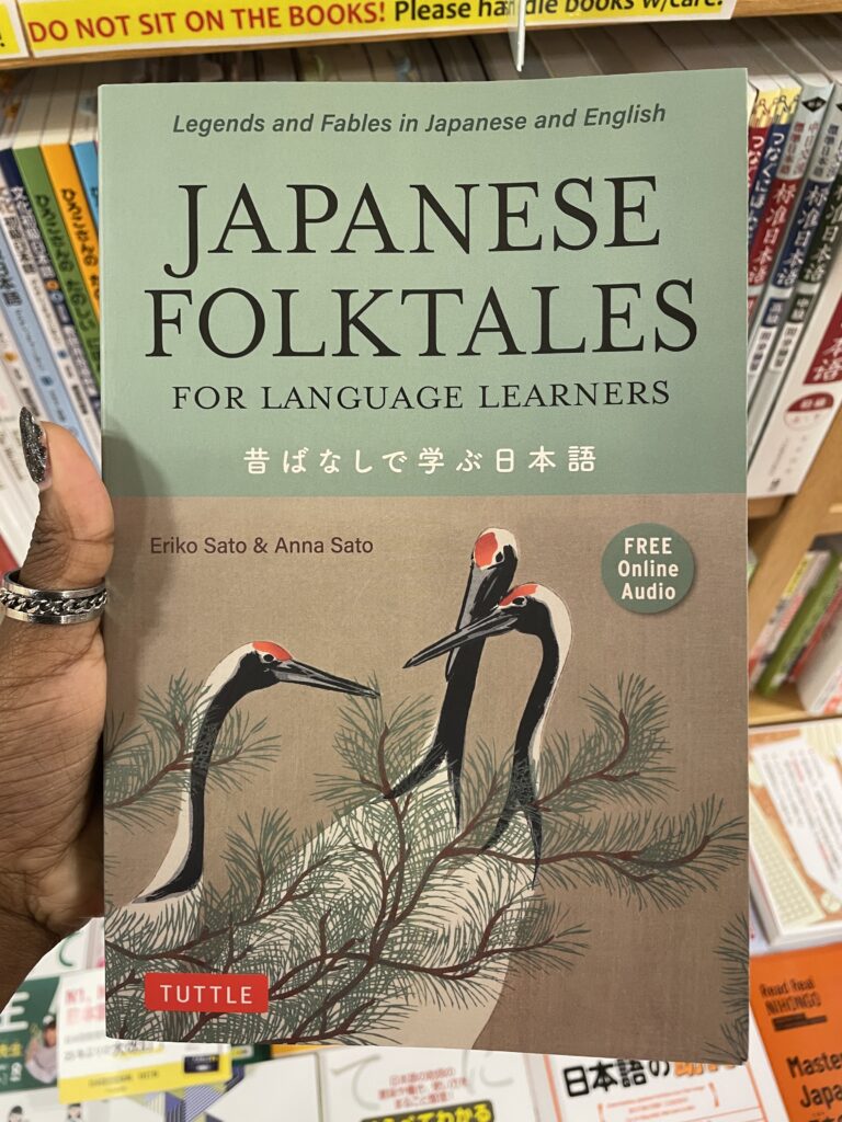 A person holding a book titled "Japanese Folktales for Language Learners," which features illustrations of cranes on the cover.