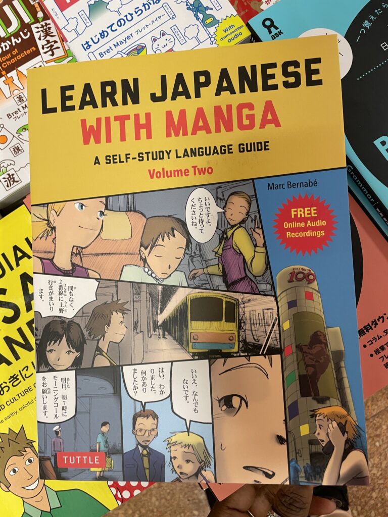 A person holding a book titled "Learn Japanese with Manga," which uses comic-style illustrations to teach Japanese.