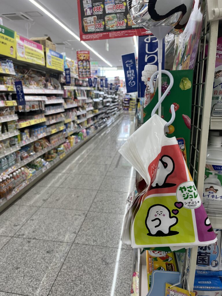 A close-up of a supermarket aisle in Japan, with a focus on colorful plastic bags hanging on a hook, and shelves stocked with various products in the background.