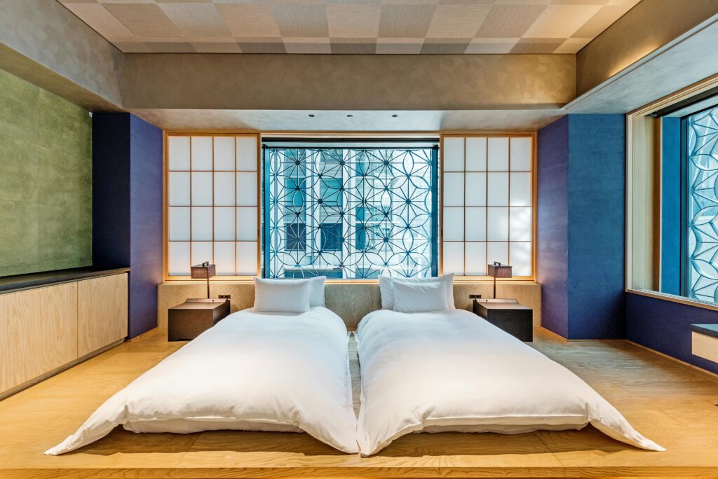 Modern Japanese-style hotel room with two single beds, shoji screens, and a decorative window.