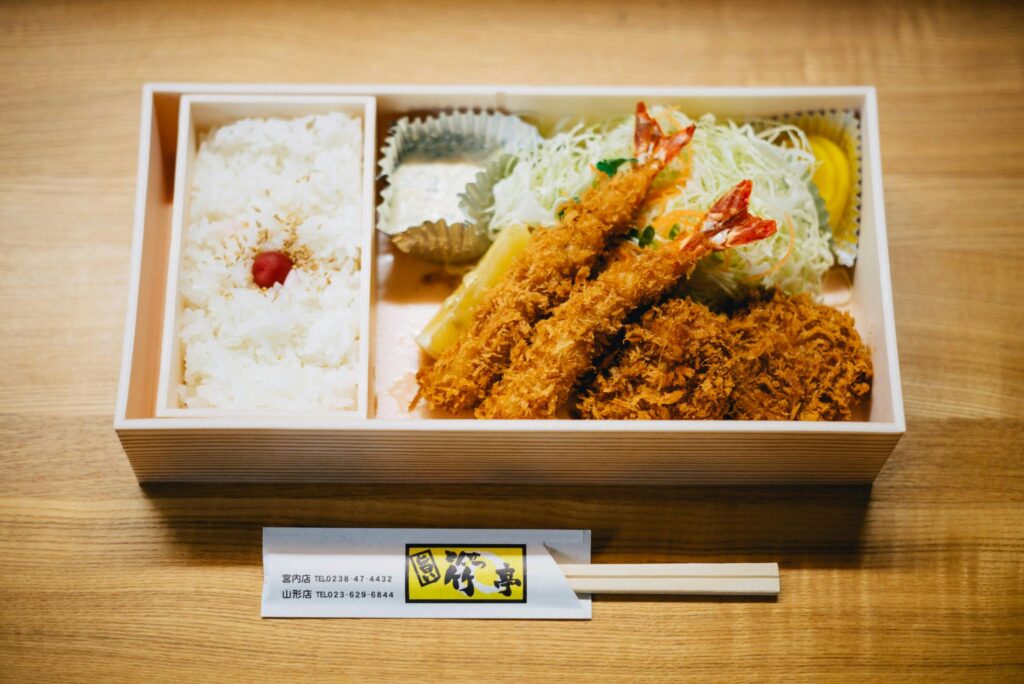 Japanese bento box with fried shrimp, rice, and vegetables.