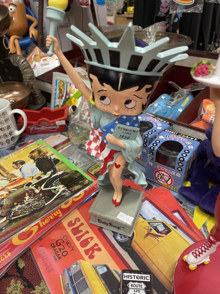 A Betty Boop figurine styled as the Statue of Liberty on display in a vintage store. 