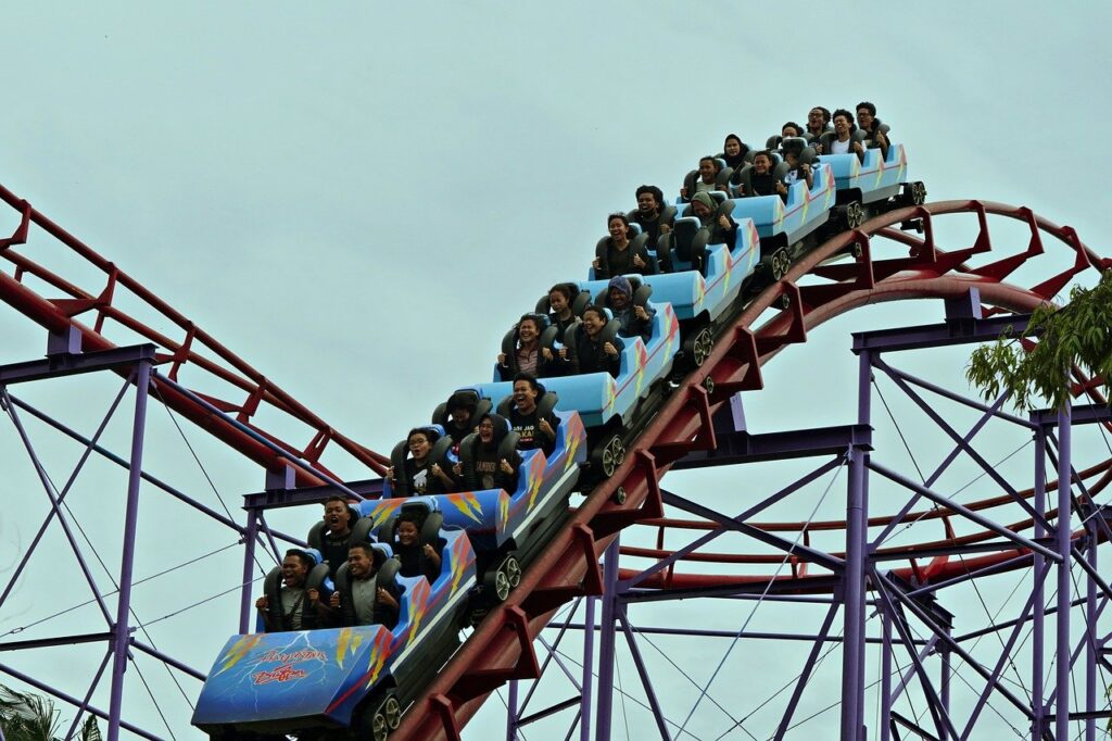 A rollercoaster filled with smiling riders experiencing an exciting drop at an amusement park.