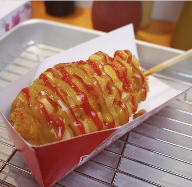 A Korean corn dog topped with ketchup and mustard, served in a paper tray in Shin-Okubo.