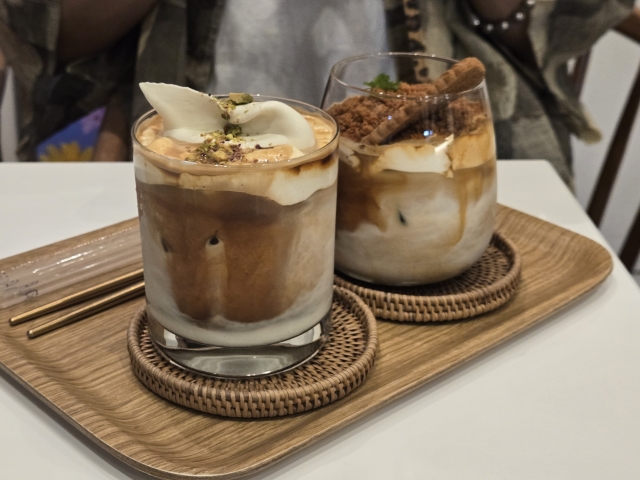 Two glasses of iced coffee topped with whipped cream and nuts, served on a wooden tray.