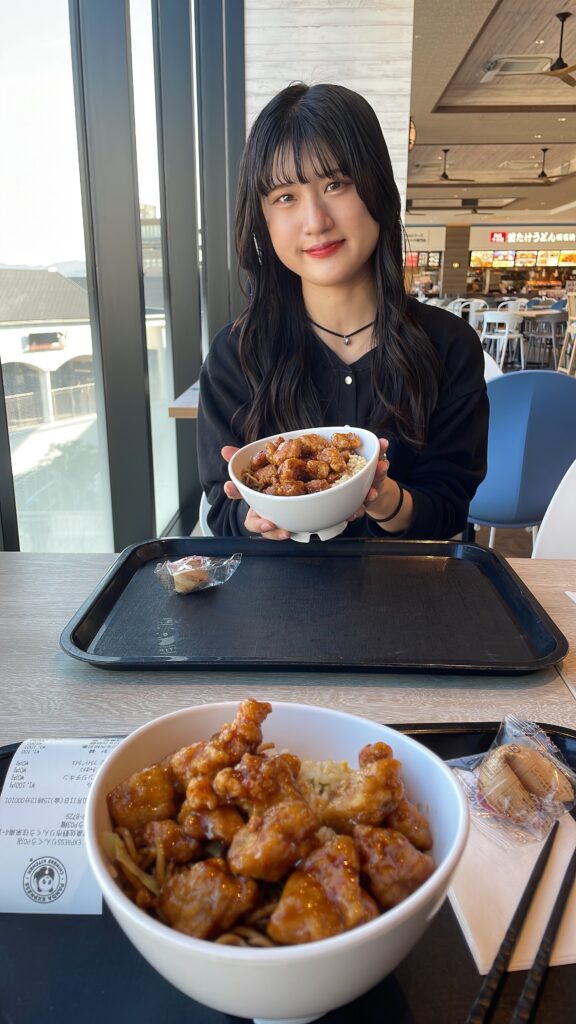 A smiling young woman holding a bowl of Panda Express orange chicken in front of her. 