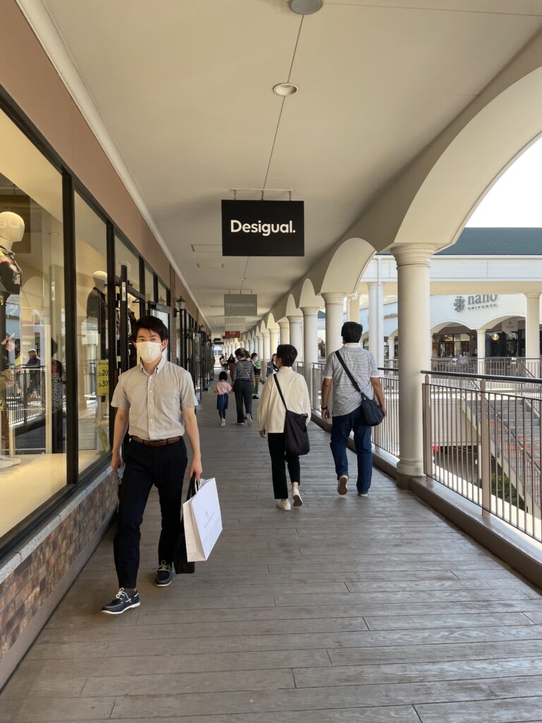 Shoppers walking along the promenade of the Rinku Premium Outlet, with visible store signage overhead.