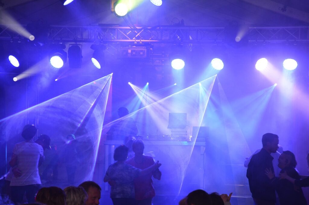 A dance floor with colorful laser lights and people enjoying a Halloween party with a DJ on stage.