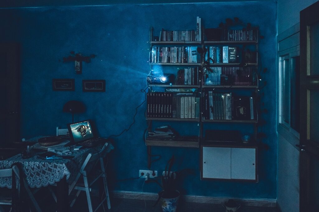 A dimly lit room with bookshelves, a desk, and a computer, creating a cozy and mysterious atmosphere.