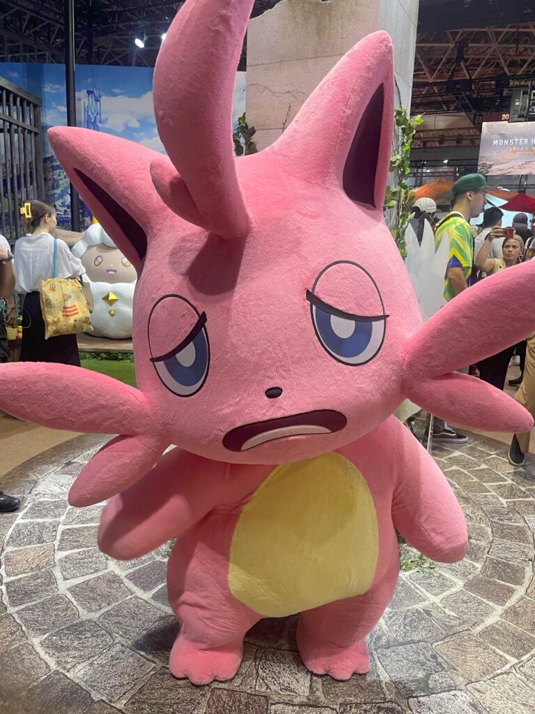 A pink mascot character posing with a sleepy expression at TGS 2024.