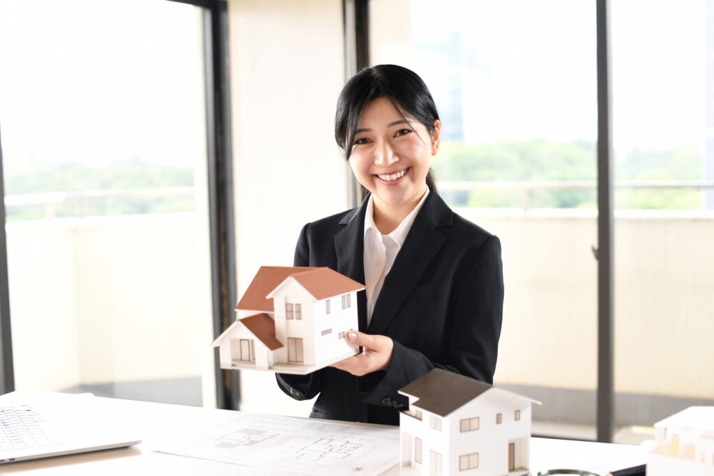 Smiling realtor holding a miniature house model, representing real estate services and Key Money.