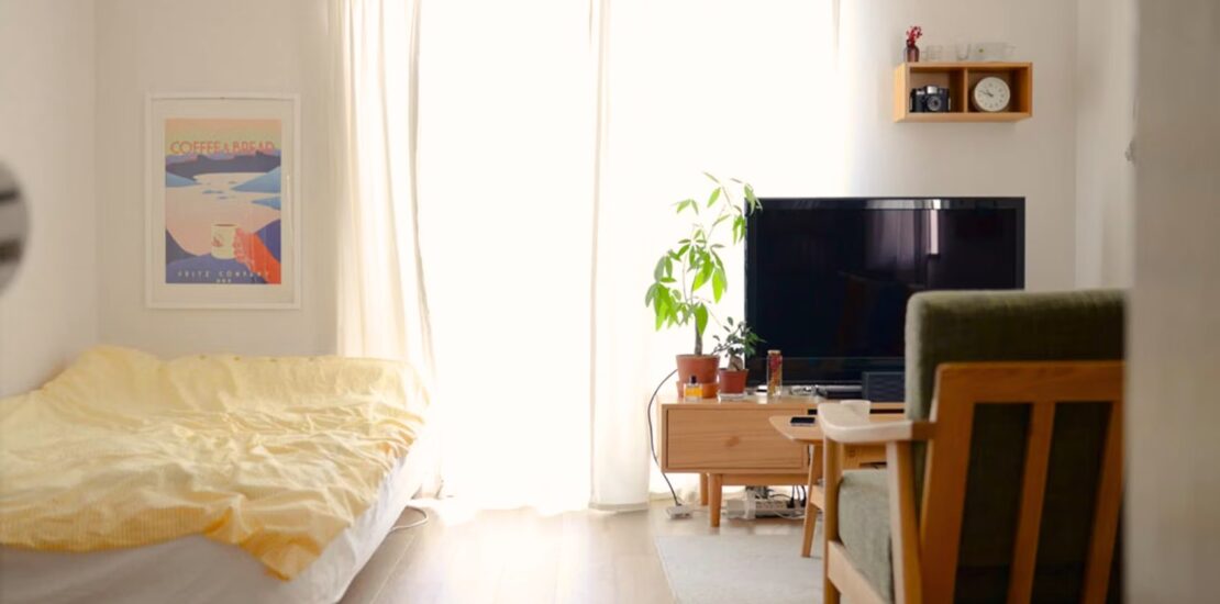 Cozy minimalist Japanese room with natural light, bed, potted plant, TV, and simple decor.