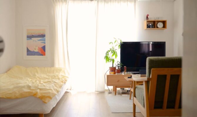 Cozy minimalist Japanese room with natural light, bed, potted plant, TV, and simple decor.