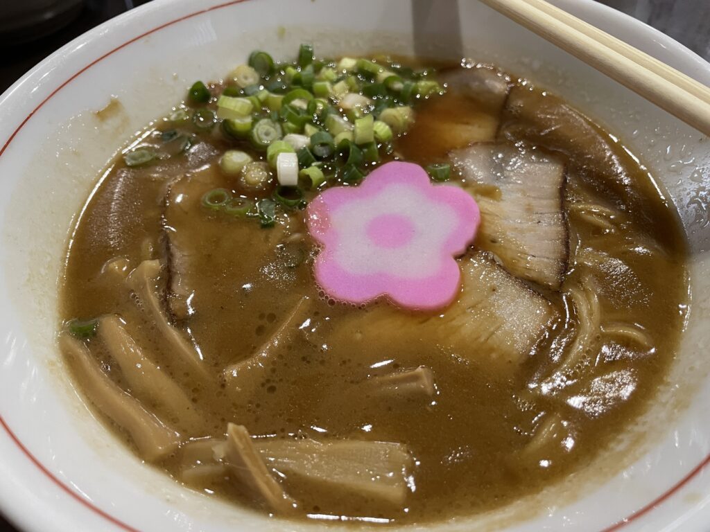 A bowl of Wakayama-style ramen with rich, savory broth, topped with green onions, bamboo shoots, sliced pork, and a decorative fish cake.