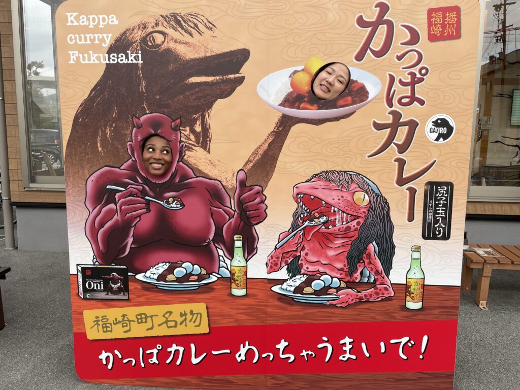  Two women posing with their faces through a cutout board featuring Kappa Curry characters in Fukusaki City.