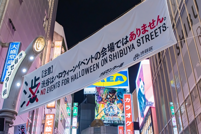  A banner in Shibuya discouraging Halloween street celebrations with bright neon signage in the background.