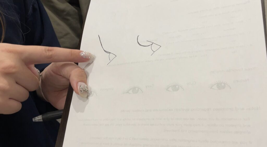 A beauty technician sketching a proposed eyebrow shape during a consultation.