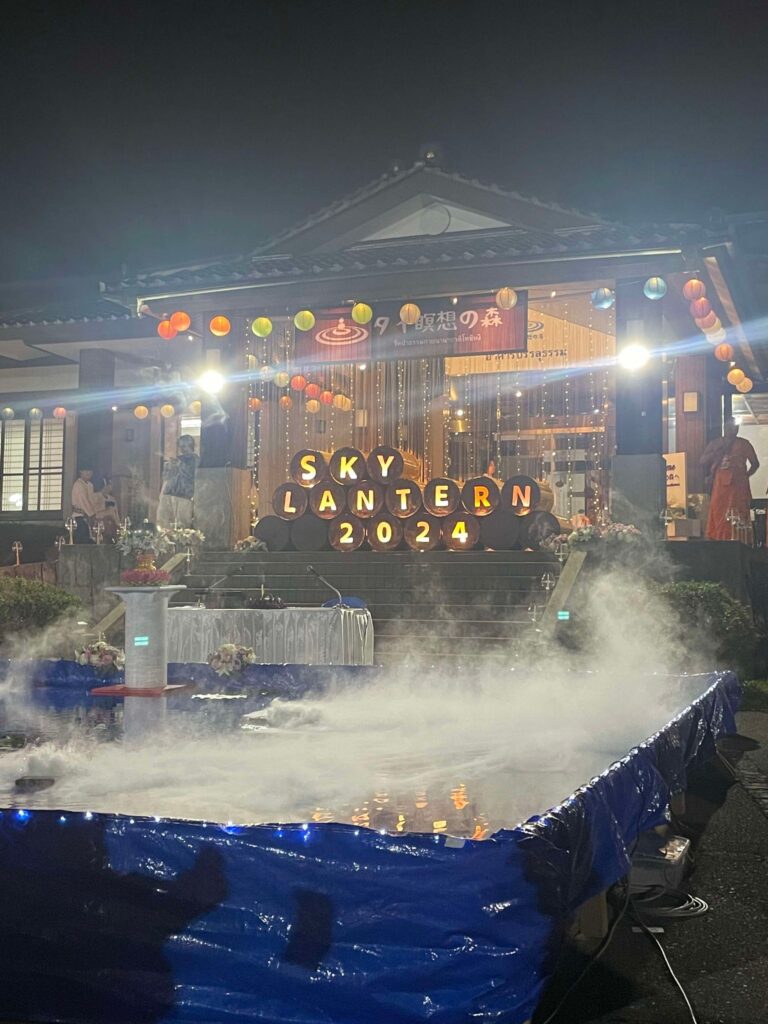 The Sky Lantern Festival stage is decorated with colorful lanterns, mist, and a sign reading "Sky Lantern 2024," creating a mystical and welcoming atmosphere for attendees.