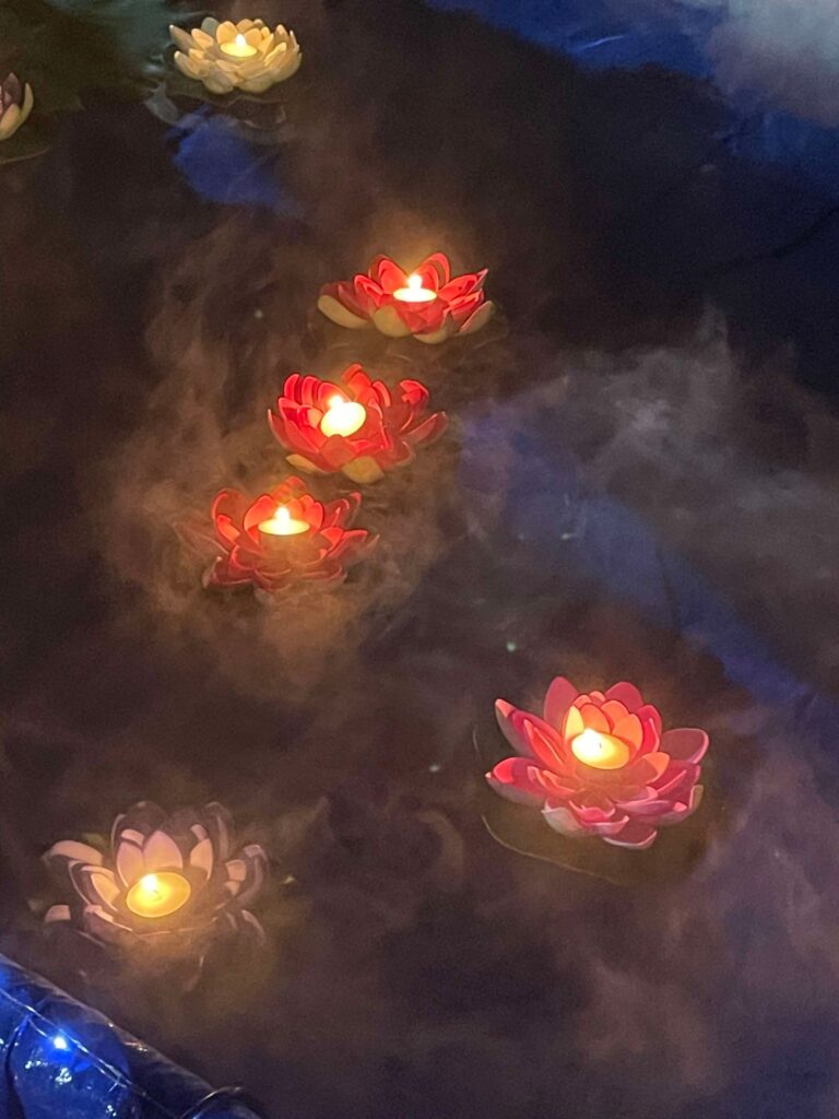 Red and white lotus-shaped candles with lit flames float peacefully on a misty pond, creating a serene and magical atmosphere at the Sky Lantern Festival.