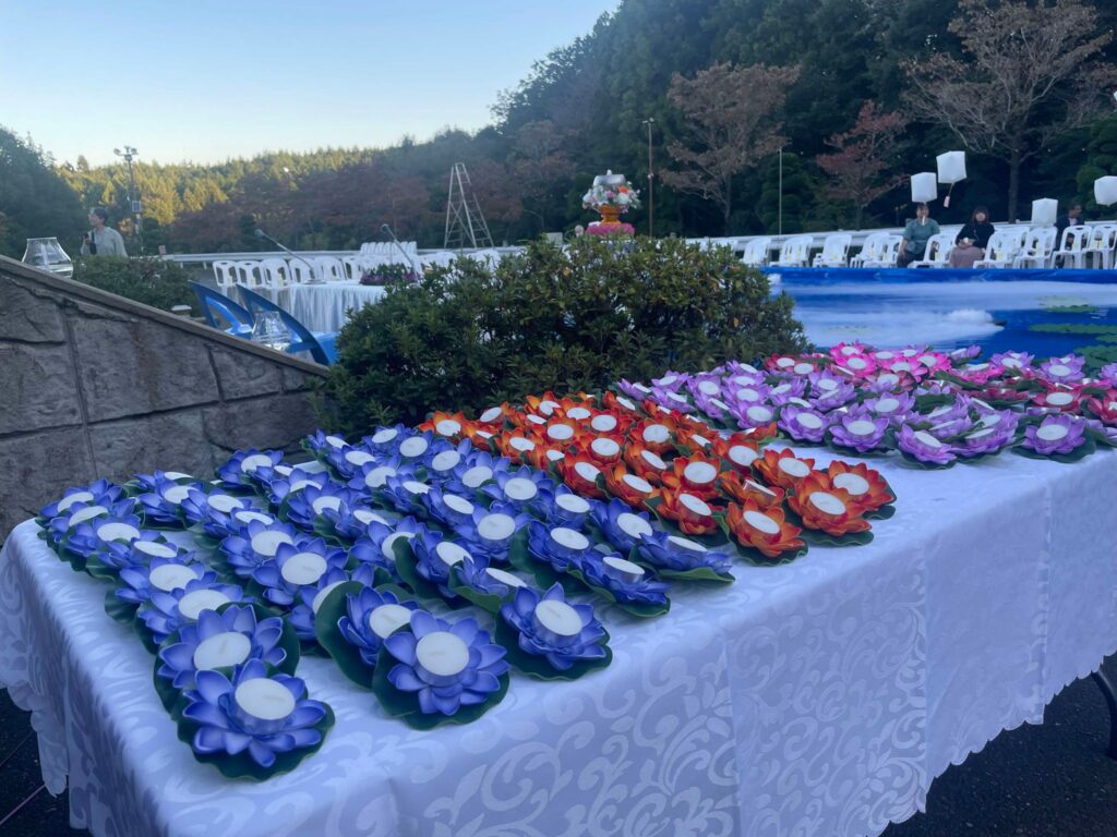 Rows of vibrant lotus-shaped candles in shades of purple, orange, and blue are neatly arranged on a white tablecloth at the Sky Lantern Festival, ready for the water lantern ceremony.