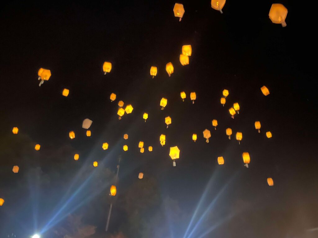 A multitude of glowing sky lanterns rise into the dark sky, filling it with warm, flickering lights, symbolizing hopes and dreams at the festival.