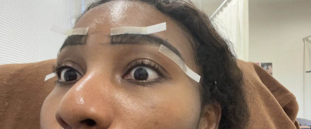 Close-up of a beauty technician holding a strip of wax with eyebrow hairs.