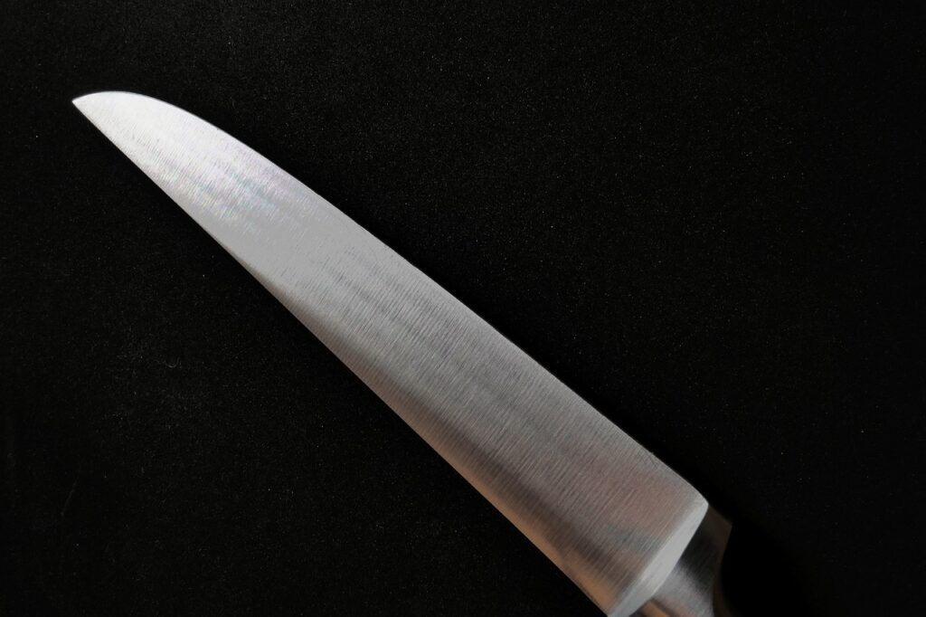 A close-up view of a freshly sharpened knife blade on a dark background, showcasing its polished edge.