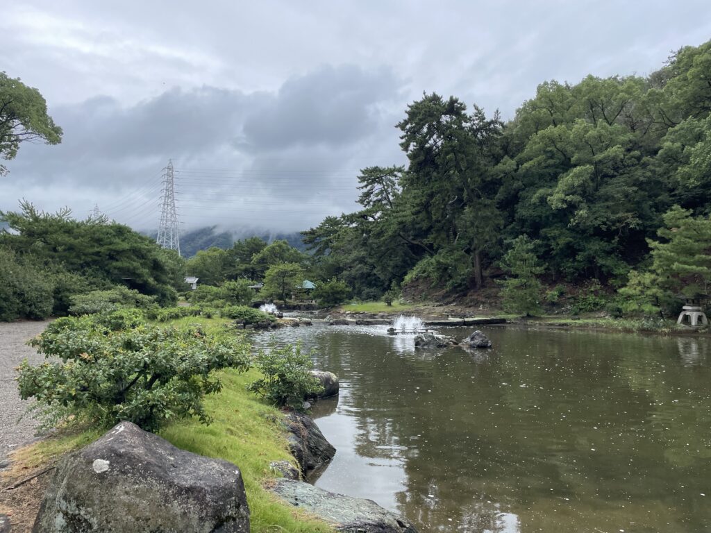 A peaceful pond surrounded by green trees and shrubs in a traditional Japanese garden at Kotonoura Onzan-sou.