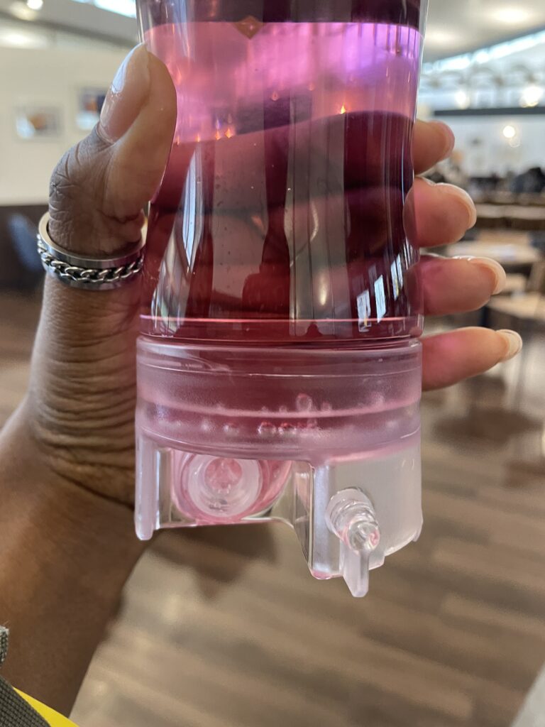 A close-up of a hand holding a customized drink in a clear plastic glass with a vibrant pink liquid.