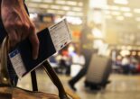 A close-up of a traveler holding a passport and boarding pass at the airport.