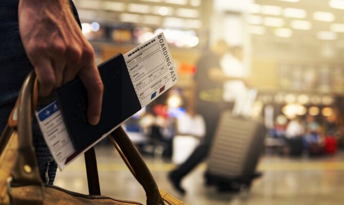 A close-up of a traveler holding a passport and boarding pass at the airport.