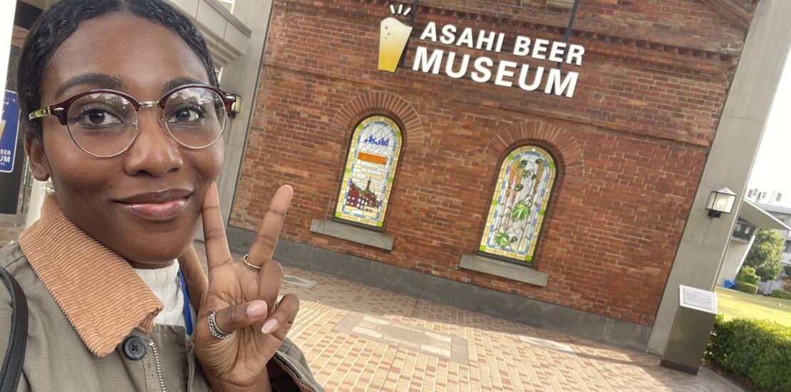 A visitor flashing a peace sign in front of the Asahi Beer Museum’s iconic brick building entrance.