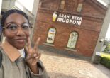 A visitor flashing a peace sign in front of the Asahi Beer Museum’s iconic brick building entrance.