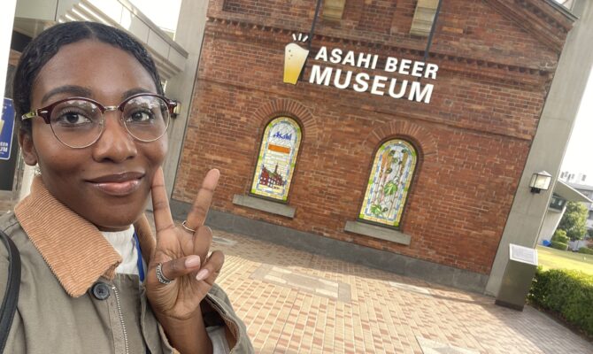 A visitor flashing a peace sign in front of the Asahi Beer Museum’s iconic brick building entrance.