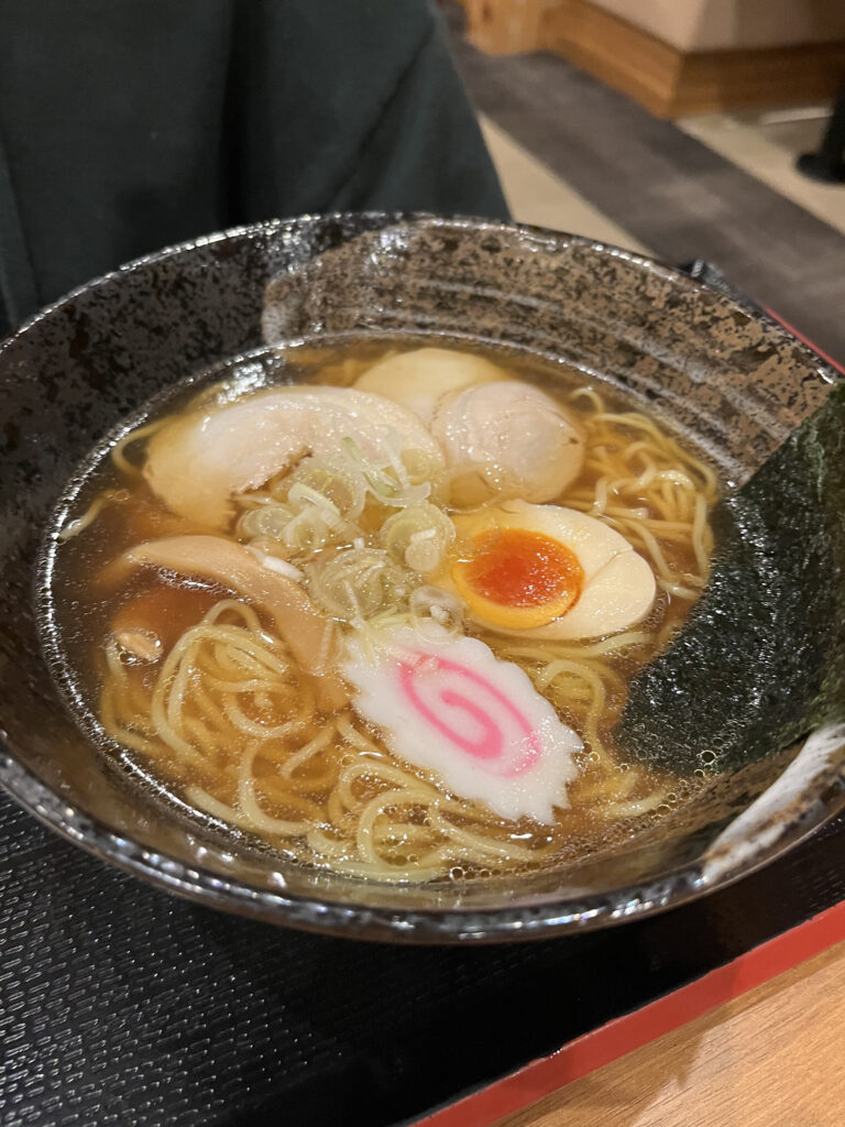 A hearty bowl of ramen topped with wontons, boiled eggs, bamboo shoots, green onions, and a sheet of nori.