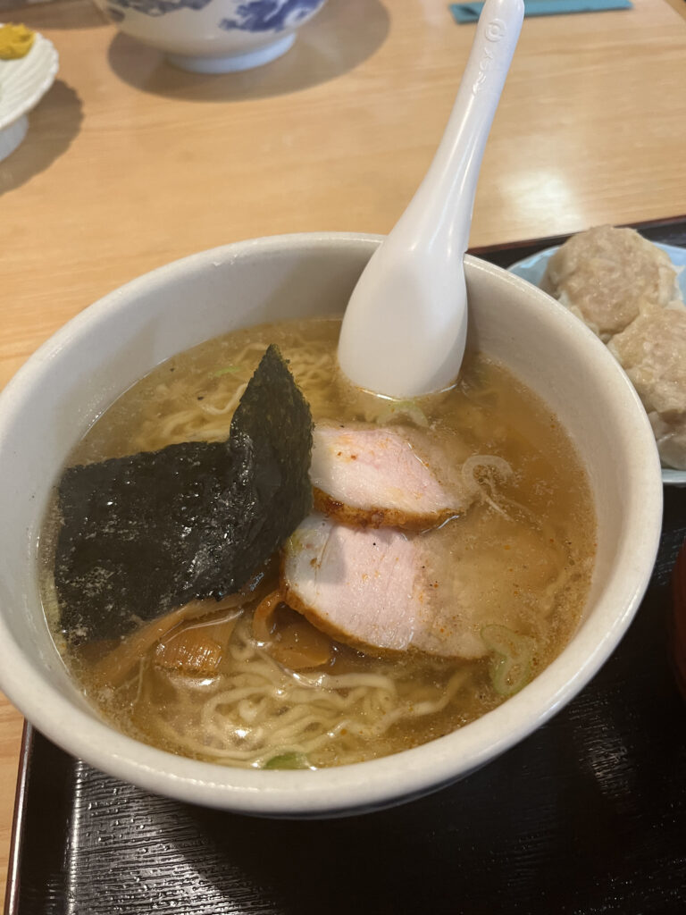 A bowl of ramen with a light, clear broth, topped with slices of roast pork and a piece of nori.