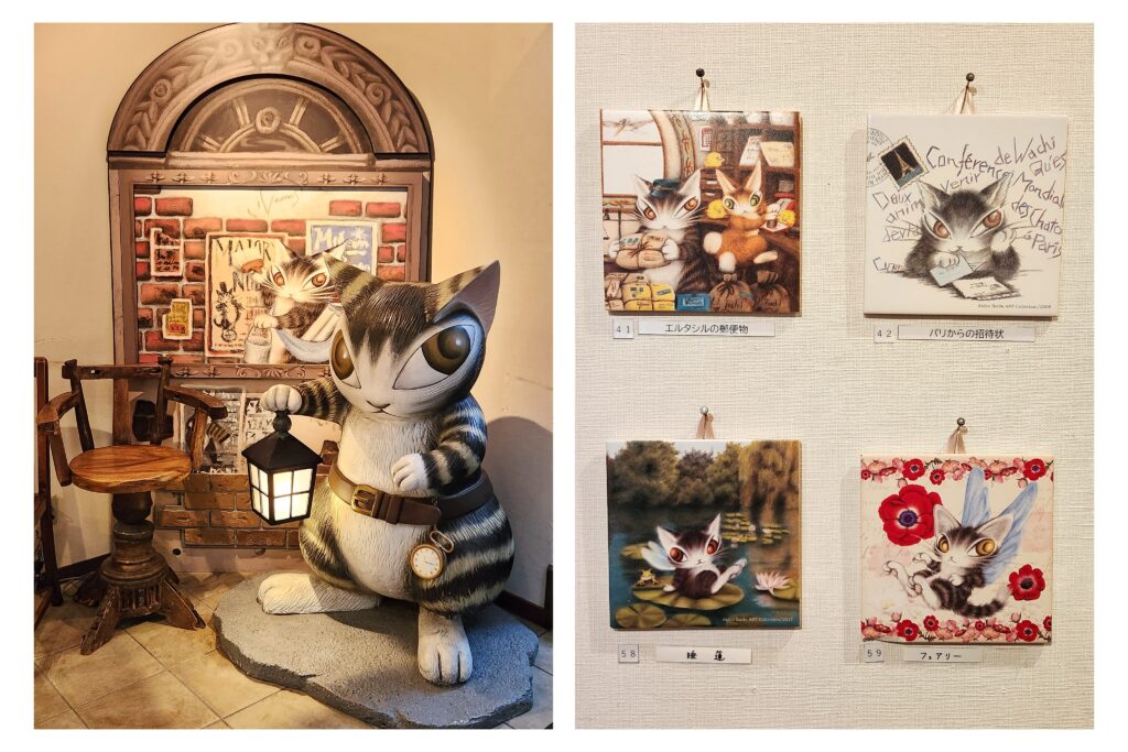 Dayan the cat statue holding a lantern, displayed inside the Kawaguchiko Konohana Museum. Artworks of whimsical feline characters hang on the walls.