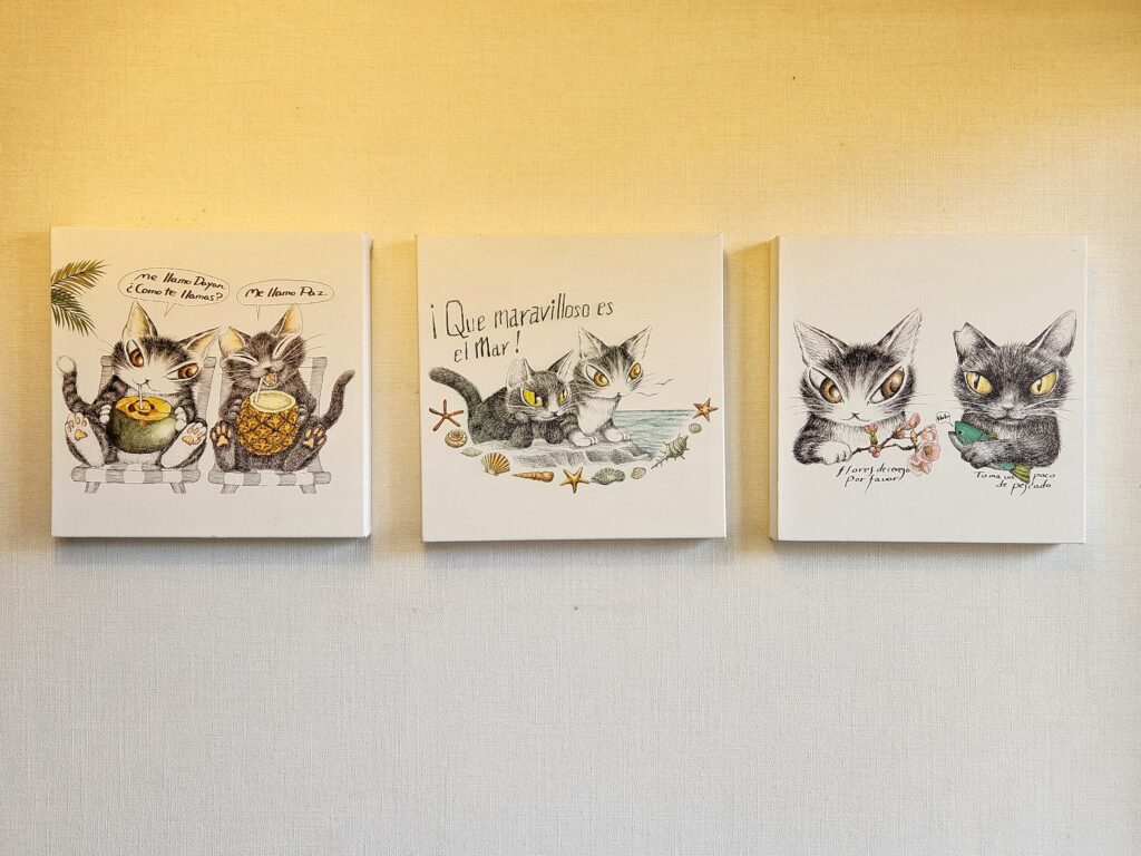 Three whimsical canvas artworks featuring Dayan the cat in playful scenarios, displayed on a white wall.