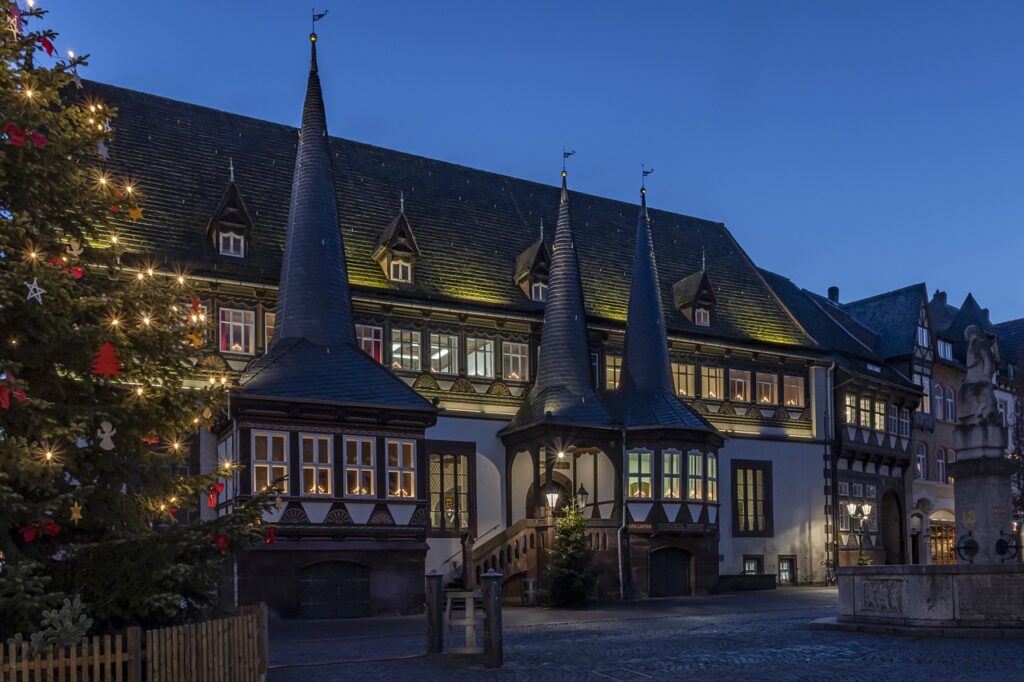 Festively lit historic building with pointed rooftops and a large Christmas tree at dusk.