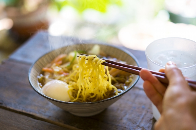 A steaming bowl of ramen with chopsticks lifting noodles, served with a soft-boiled egg and fresh vegetables on a rustic wooden table.