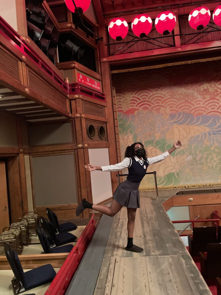 Visitor posing joyfully on the main stage at the Kyoto Geisha Museum.