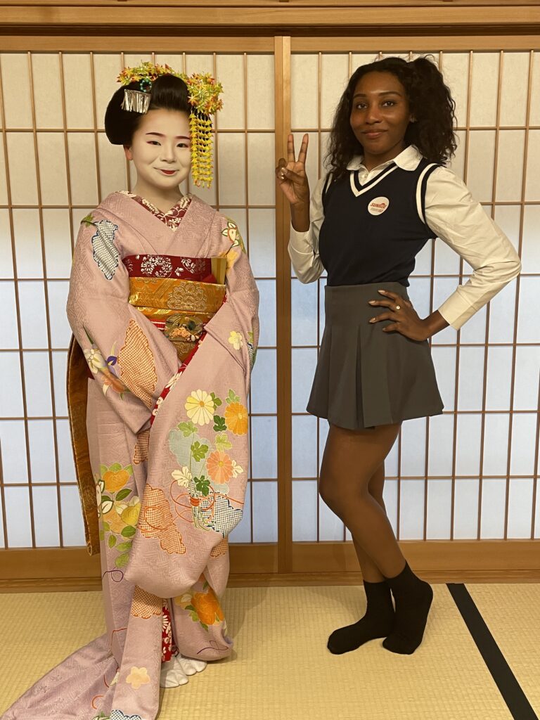 A maiko in pink kimono posing with a visitor inside a traditional Kyoto house.