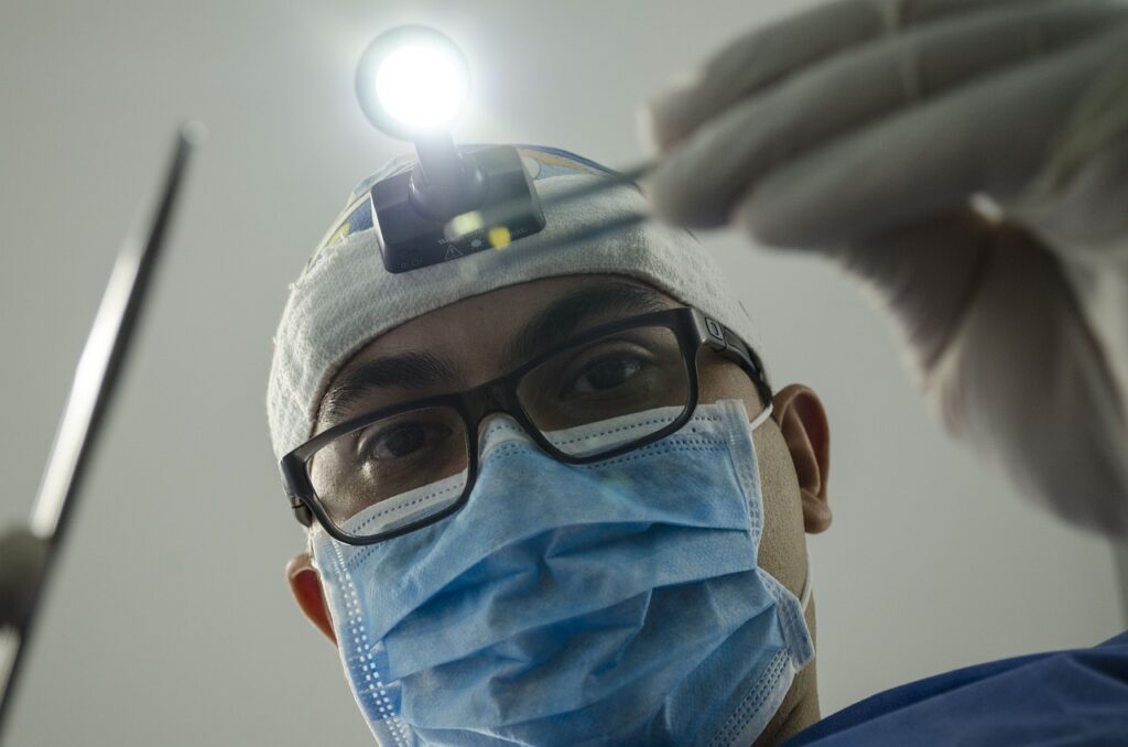 A dentist wearing a surgical mask and headlamp, holding dental instruments, ready to examine a patient.