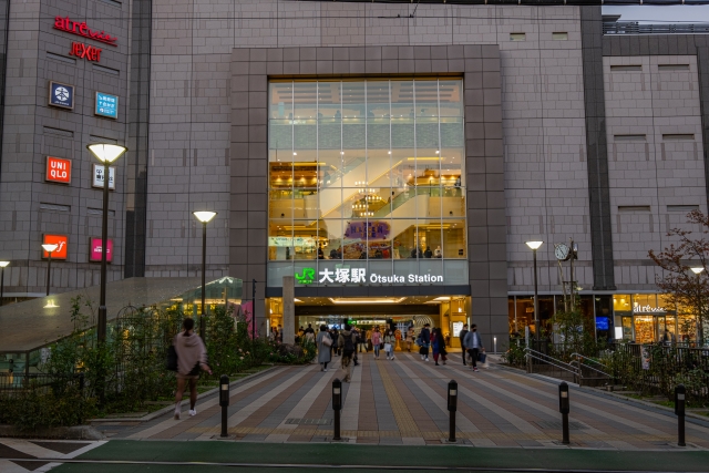 The brightly lit exterior of Otsuka Station in Tokyo at dusk, bustling with pedestrians.