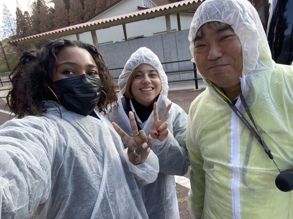 Three people in white protective suits smiling for the camera outdoors.