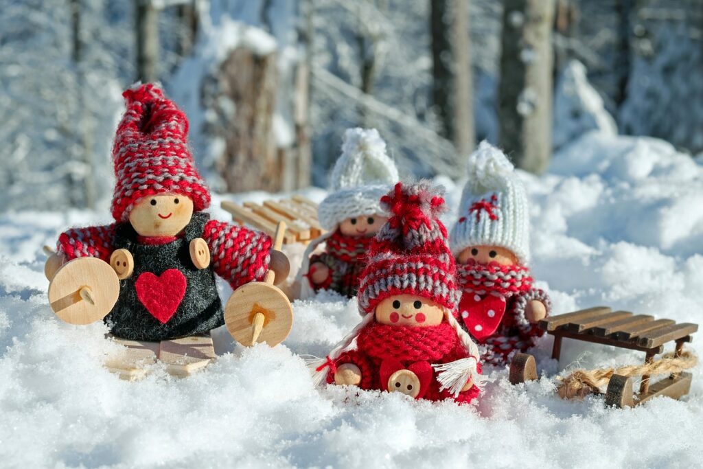 Wooden Christmas figurines dressed in red and white, sitting in snow alongside small sleds.