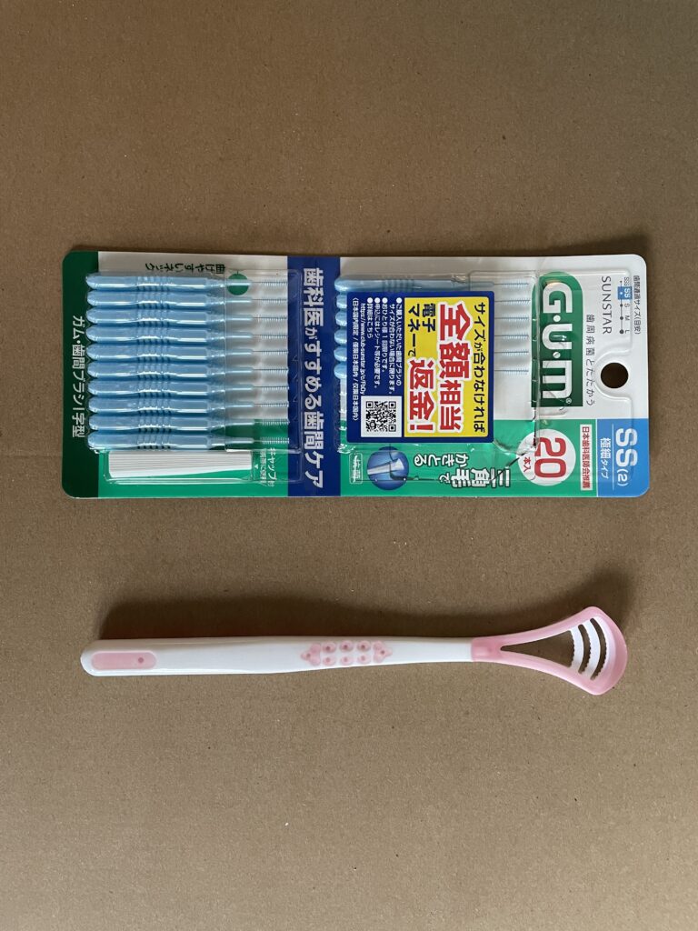 Gum floss and a pink tongue cleaner on a brown surface, essential tools for oral hygiene.